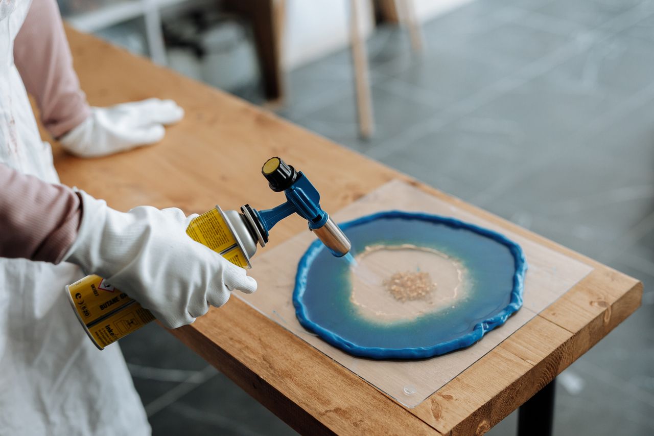 About Close-up of hands using blowtorch in resin art on wooden table.